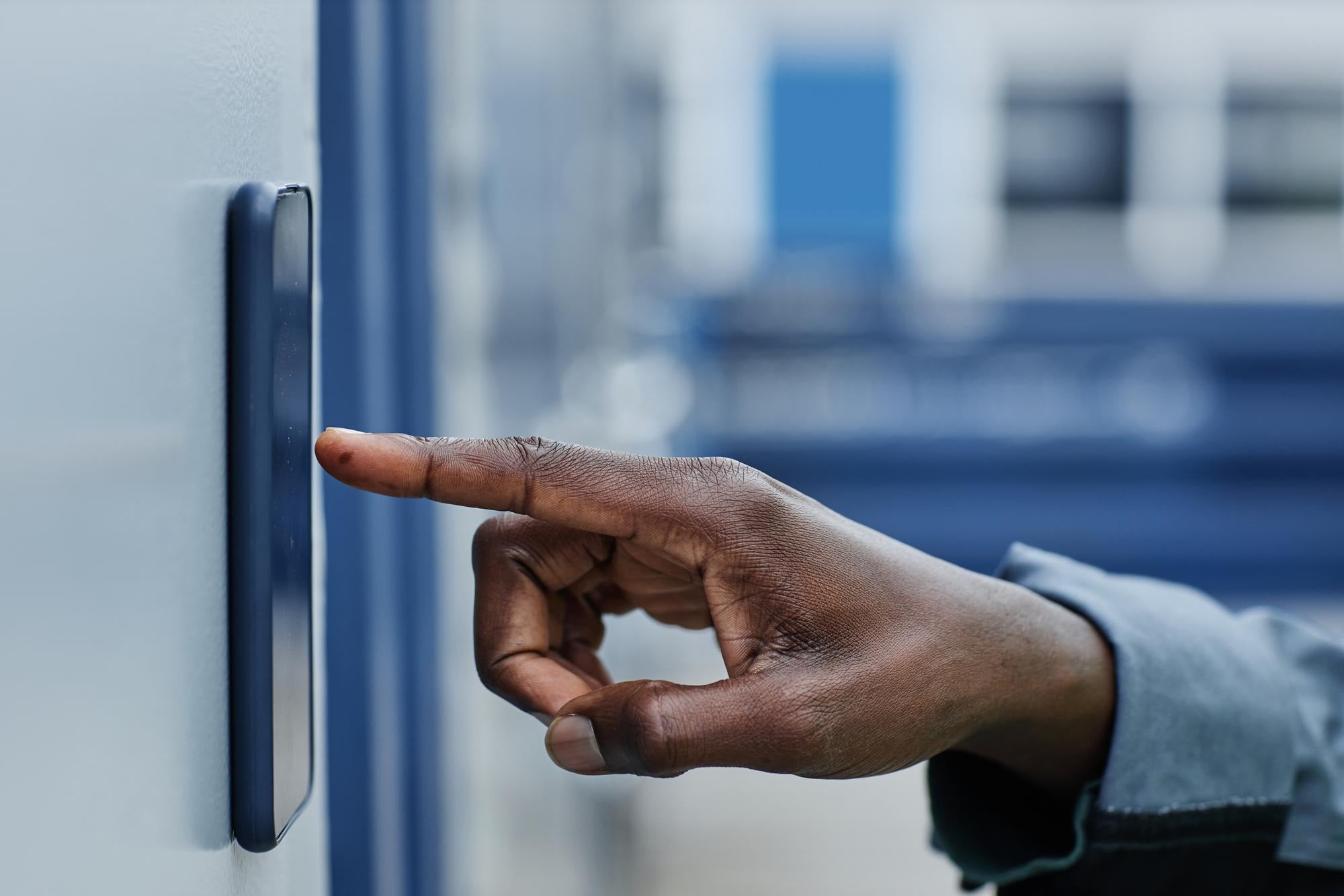 A finger about to tap a wall-mounted access reader beside a door