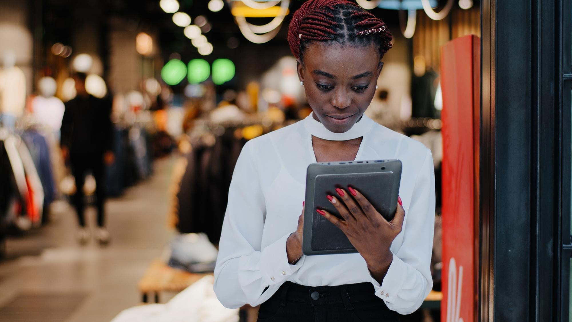 A woman reading a tablet at the entrance of a busy store