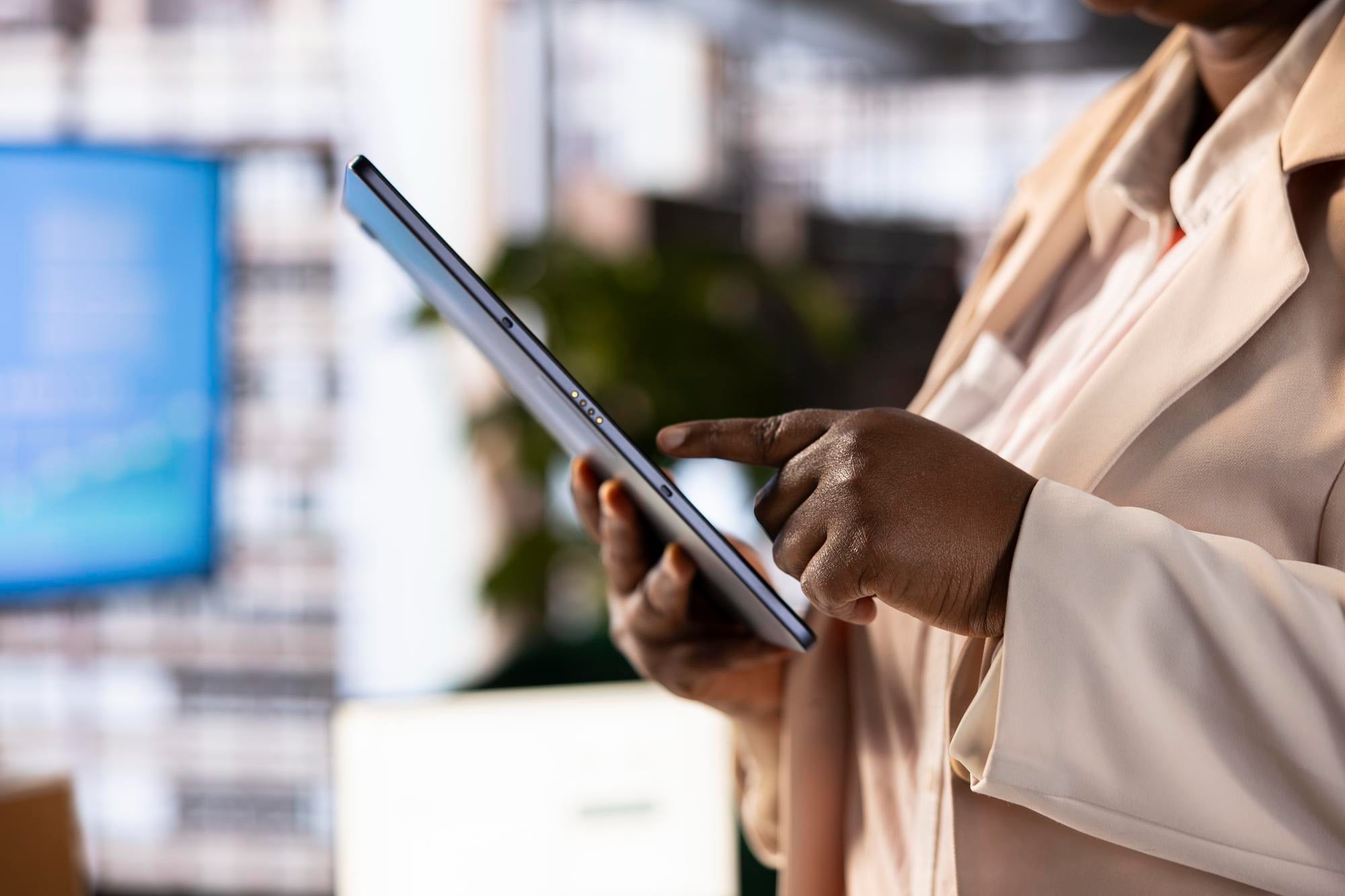 A woman in a light blazer tapping a tablet in a bright office