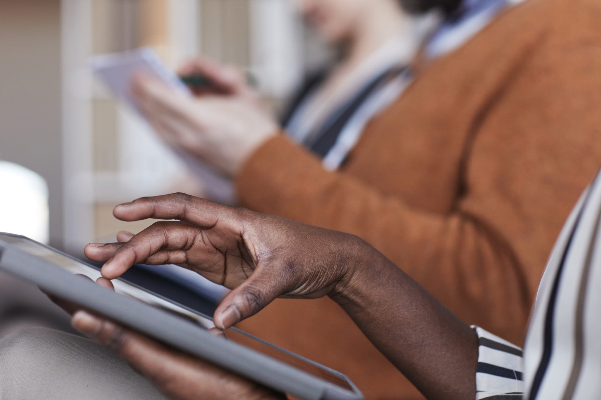 People in a waiting area filling in forms, one on a tablet